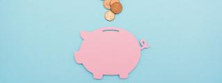 Pink piggy bank on blue background with coins above the opening