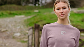 Woman wearing pink Love not Laboratories jumper in field